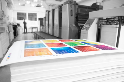 A colourful printed calendar sheet in a black and white press room.